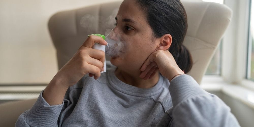 A woman receiving respiratory therapy from a healthcare professional using a nebulizer mask.
